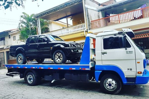 Caminhonete preta sobre plataforma de caminhão guincho azul e branco.