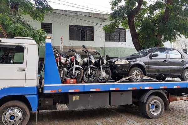 Três motos e um carro escuro sobre a plataforma de um caminhão guincho.